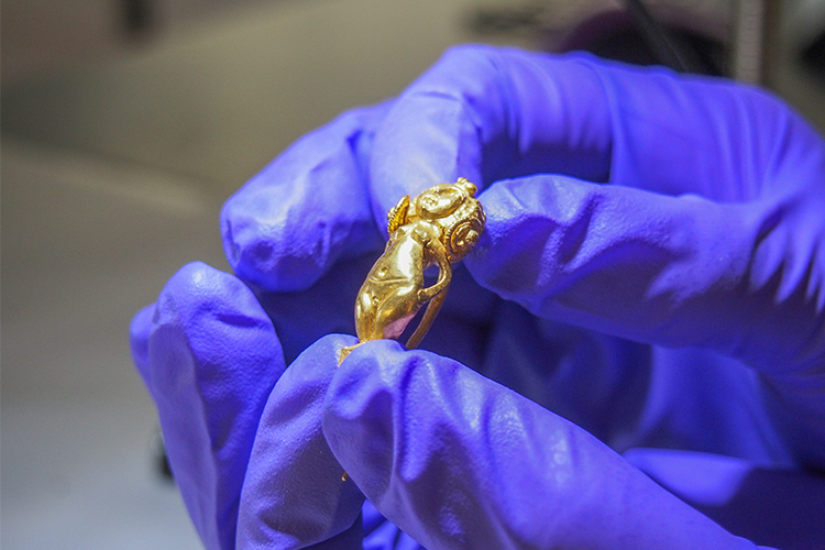 Close up of gloved hands holding a small gold figurine.