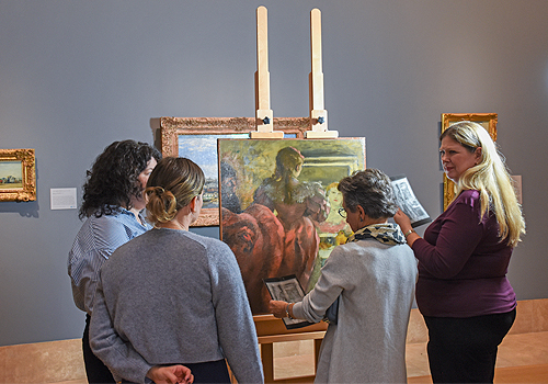 Four individuals looking at a painting on an easel.