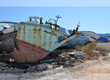 Four dilapidated fhishing vessels with debris sitting on sand and rocks.