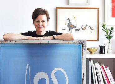 Alanna Cavanagh holding a blue painting standing in their studio.