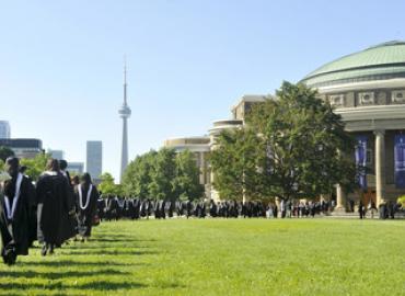 Students in academic dress walking on grass towards COnvocation Hall, CN Tower in background